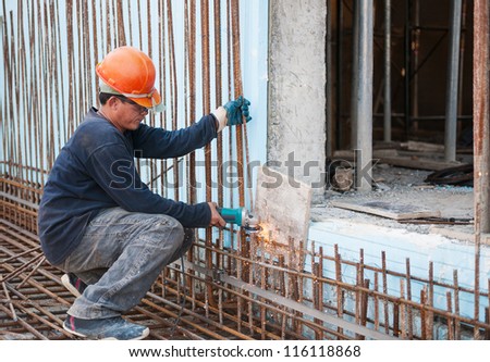 Authentic construction worker cutting steel rods with electrical saw