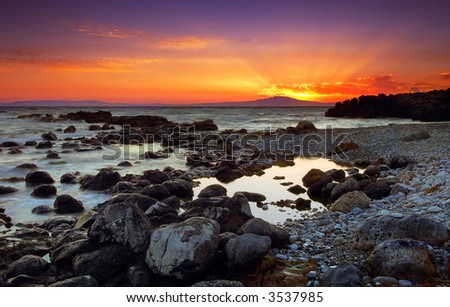 Image shows a spectacular sunset over a rocky seascape, in Mani peninsula, southern Greece