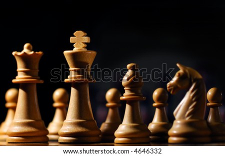 Image shows chess pieces around the white King, photographed from a low angle and with selective focusing on the king.