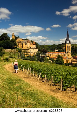 Image shows a blond country girl walking on a gravel road in a village in the French wine-making region of Beaujolais