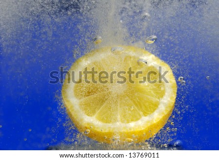 Image shows a lemon dropped in a fizzy drink against a blue background