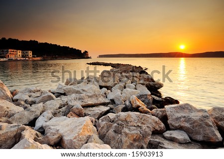 Image of a sunset in the town of Pylos, southern Greece, with rocks in the foreground and the island of Sfaktiria in the background
