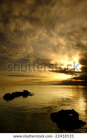 Spectacular golden sunset over silhouetted sea rocks. Room for text on top.