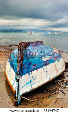 Picture from a fishing village showing an upside down and heavily weathered fishing boat stranded on the beach. Room for text on top.