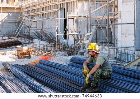 Construction worker resting on piles of reinforcement steel bars, in a busy construction site