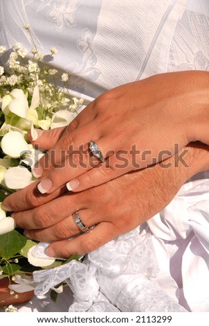 Husband and wife showing their wedding rings surrounded by the bride\'s bouquet.