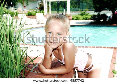 Cute little girl playing in the garden and standing next to a brick wall by the pool.