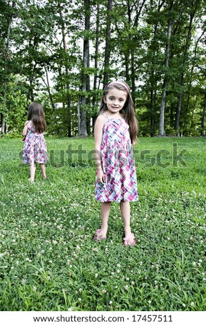 Two little girls standing in a garden with identical dresses.  One facing front and the other facing back.