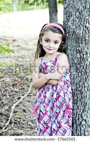 Young girl standing with arms folded next to a tree.