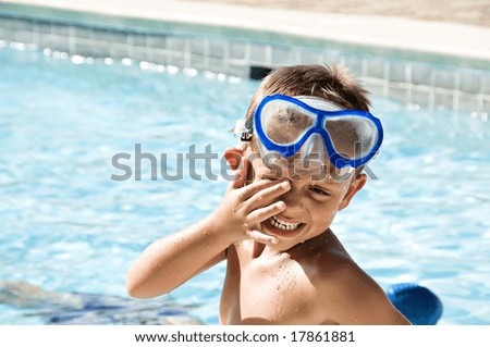 Young boy rubbing his eyes wearing goggles after a swim in the pool.