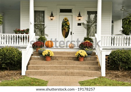 A beautiful front porch decorated for fall with sunflowers, mums, pumpkins, pansies, and a jack-o-latern