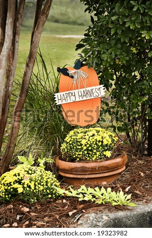A fall display with a Happy Harvest banner pumpkin and fall mums.