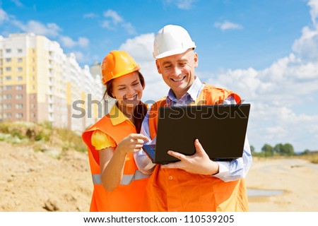 female and male construction workers looking at laptop and smiling