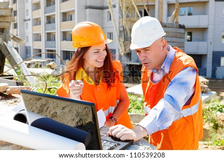 Female architect and construction worker looking at laptop together against construction