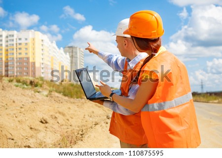 A male manager on a construction site wearing a hard hat and talking with his  female colleague and points at home
