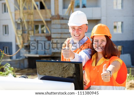 female and male construction workers looking at laptop and smiling