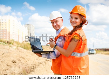 female and male construction workers looking at laptop against the backdrop of houses under construction