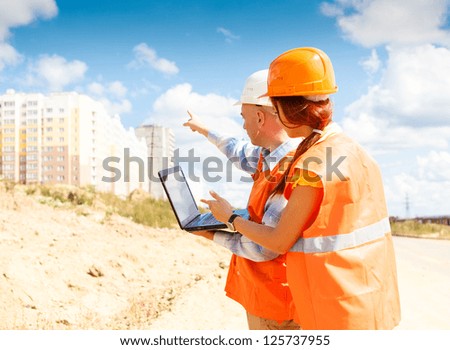 female and male construction workers looking at laptop against the backdrop of houses under construction