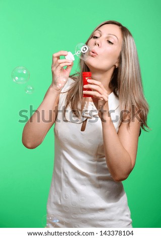 cheerful girl inflates soap bubbles on a green background