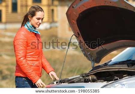 sad girl looking at a broken down car with the hood open