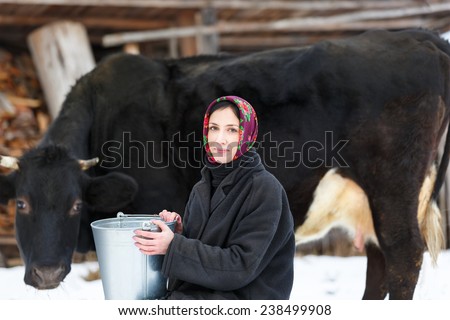 Farmer woman in traditional Russian dress milking a cow in winter yard
