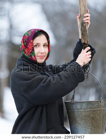 woman in winter clothes in a bucket at  well
