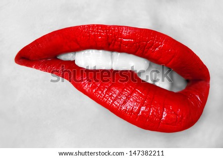 Sensuous woman biting red lips on gray