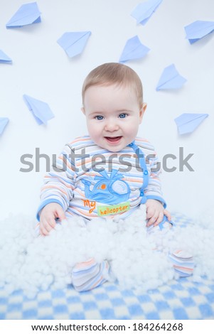 Cute smiling baby in nursery sitting on checkered plaid. Paper origami planes on background