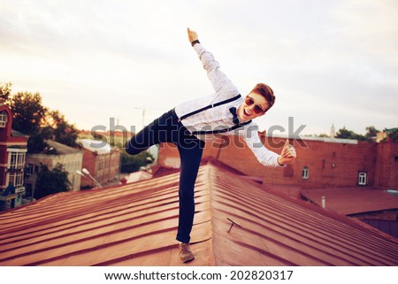 Young bold girl woman in hipster clothes, jumping on the roof, dressed like a boy man in a shirt, bow-tie, suspenders and pants trousers