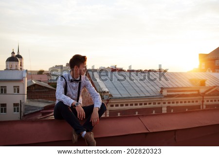 Young bold girl woman in hipster clothes, sit on edge of roof, dressed like a boy man in shirt, bow-tie, suspenders and pants trousers