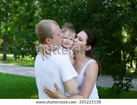 Happy family outdoors  mum and dad hold and kiss baby