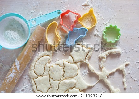 Thin dough on table with colorful plastic cake molds, raw cookies and kitchen equipment rolling pin and sieve