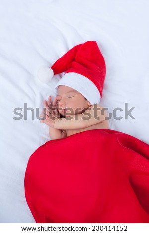Soft portrait of newborn baby boy kid in red santa claus hat, sleeping on white background. Focus on close eye, cheek and hand. Merry christmas and happy new year greeting card.