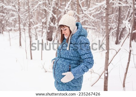 Young beautiful pregnant woman, walking in park and breathing fresh winter air