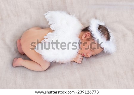 Soft image of cute newborn baby sleeping on grey background covered with white angel\'s wings and halo nimbus made of feathers, focus on close eye, ear, hear, halo and plumage