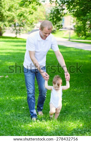 Father dad parent holding baby\'s hands outdoors in summer garden, first steps of a boy
