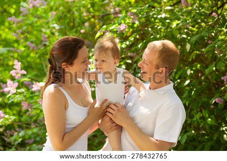 Father dad and mum mother parent holding baby boy outdoors in summer garden, talking together