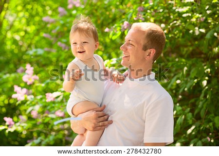 Father dad parent holding baby boy outdoors in summer garden, talking together