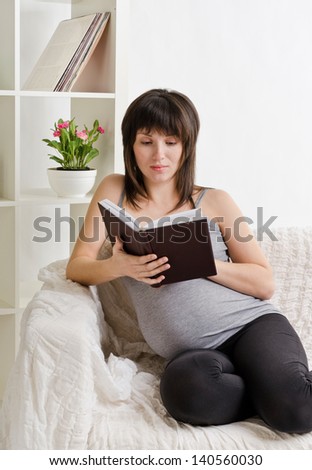 the young beautiful pregnant woman read a book on a sofa at home