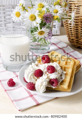 Composition with a glass of the milk, a raspberry, a waffles and a bouquet of wild flowers