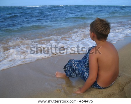 Preteen, adolescent boy waiting for the surf to roll in to the shoreline.