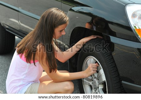 A young teenage girl checks the tires on her car