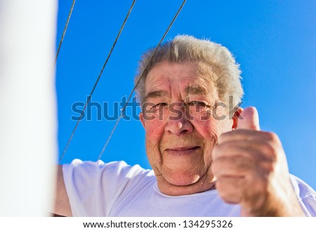 Senior lifts the thumbs up in bright blue sky