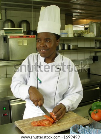 Black female chef slicing tomatoes on a wooden cutting board