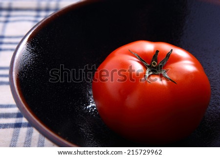 Fresh tomato in dark plate on white-blue table cloth as background
