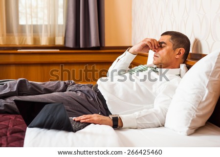 Businessman lying in bed in hotel room and thinking