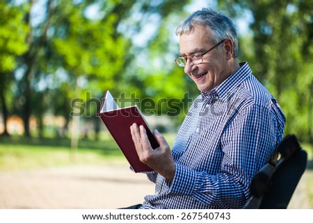Portrait of happy senior man reading a book in park