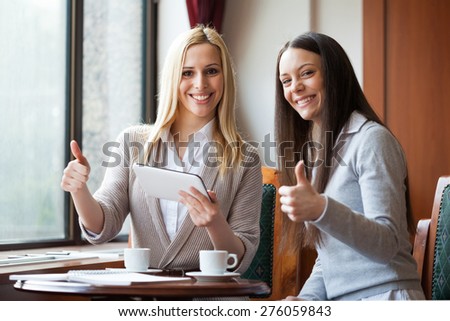 Two women drinking coffee and using digital tablet in cafe