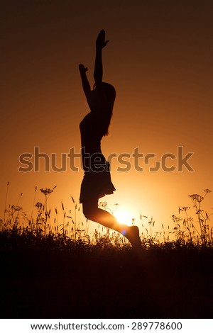Silhouette of happy woman jumping in sunset
