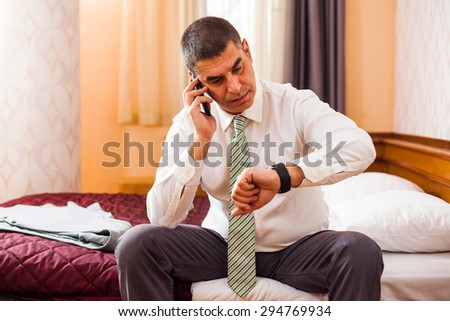 Businessman looking at his watch and talking on phone, he is ready for work.